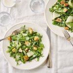 Twee bordjes staan op tafel met een wit linnen tafelkleed. De bordjes zijn fris van kleur door de verse groene groenten, de goudgebakken croutons zien er heerlijk uit.