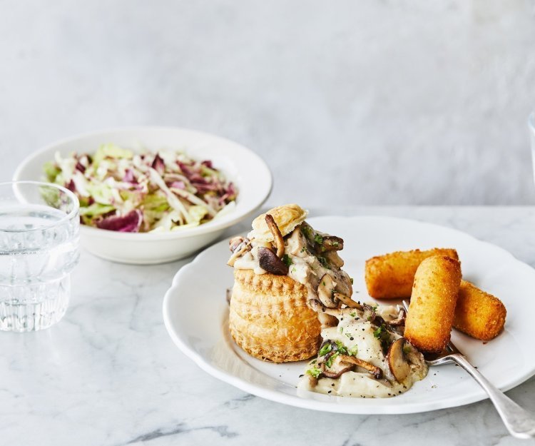 Een heerlijke vol-au-vent in met goudgele kroketten op een bord geserveerd. Er ligt een vork op het bord en het slaatje op basis van radicchio staat bovenaan, dat zorgt voor extra kleur. 