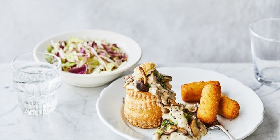 Een heerlijke vol-au-vent in met goudgele kroketten op een bord geserveerd. Er ligt een vork op het bord en het slaatje op basis van radicchio staat bovenaan, dat zorgt voor extra kleur. 