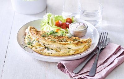 Een heerlijke omelet ligt op een wit bord. Het is een luchtige omelette die we combineren met verse kruiden en kaas. We voegde ook nog wat sla en tomaatjes toe aan het bord voor een extra portie kleur en groenten. 