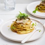 Op tafel staan twee borden, elk met een torentje van aardappelschijfjes, venkel en hierop een stukje pladijs. We werken af met kappertjes, olijfolie en wat venkelgroen. Er ligt een witte servette langs en een wit vork. 