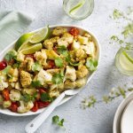 Aloo gobi is een Indiase curry van aardappel en bloemkool. Wij deden er nog stukjes kip bij. Deze rijkgevulde schotel van groenten en kruiden staat op tafel met een grote witte lepel bij. Voor de afwerking werd deze schotel gepresenteerd met korianderblaadjes en limoenpartjes. 