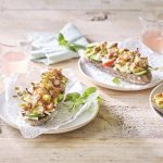 Er staan 3 bordjes klaar op een houten tafel. De ideale lunch om te benuttigen buiten in de zon. De halve broodjes zijn belegd met kruidige kip en verse groentjes. 