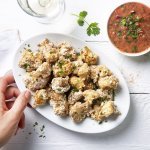 Krokante bloemkoolroosjes als aperitiefhapje, liggen klaar op een ovaal wit bordje. Er staat een pittige tomatensaus langs om te dippen. Tijd voor de apero te starten. 