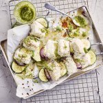 Klaargemaakte brochettes liggen in een grijze ovenschaal te blinken. De spiesjes bestaan uit stukjes heek, courgette en rode ui. Er staat een glazen potje naast met huisgemaakte dragonpesto.