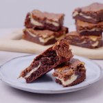 De browniecheesecake ligt op een bordje aangesneden. Dit is eigenlijk een brownie in combinatie met cheesecake, zo verkrijg je een marmereffect in je brownie door het mengsel met de roomkaas. 