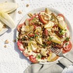 Op tafel ligt een wit tafelkleed met gaatjespatroon. Hierop staat een bord met de tomatencarpaccio, witloof en witte dressing op basis van ricotta.