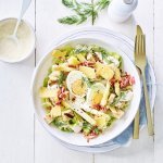 Een rijkgevulde salade staat klaar op tafel. Het witte bord is gevuld met sla, gekookte eitjes, stukjes asperges en kaasschilfers. Dat is de lente proeven in je bord, als je het mij vraagt!