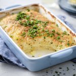 De ovenschotel met gratin staat op tafel, hij heeft een lichtblauwe kleur. De aardappelschijfjes zijn lekker crispy gebakken, doordat we ze in de oven klaarmaken met minder room. De ovenschotel is afgewerkt met verse fijngehakte bieslook.