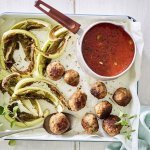 Gegrilde bloemkoolbladeren liggen op de ovenschaal met gehaktballetjes en tomatensaus in een sauspannetje. 