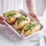 3 gepofte aardappelen met pesto, erwtjes en rucola liggen in een witte ovenschaal. De vrouw wil de ovenschaal plaatsen op tafel.