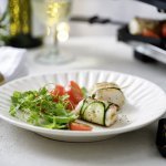 Twee pakjes liggen op een wit bord. Het pakje is gemaakt van een stukje vis verpakt in een sliertje courgette. We serveren dit feestelijk gerechtje met een frisgroene kruidensla en kertomaatjes.  