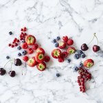 Aardbeien, frambozen, blauwe bessen, rode bessen en kersen liggen op een marmer aanrecht. Klaar om te verwerken in een homemade confituur. 