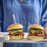 Een vrouw staat in beeld met haar romp draagt een plateau met hierop twee hamburgers. De hamburgerbroodjes hebben een mooi goudgele kleur, ze werden gemaakt met aardappelpuree in het deeg. Verder zijn de burger belgd met een schijfje vlees, kaas, tomaat, sla en saus natuurlijk. 