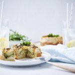 Kleine quiche van brood met broccoli en paprika op wit bordje met houte bestek langs het bord. Er staan ook twee waterglazen met een schijfje citroen en kartonnen rietje in.