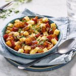 Een bord gevuld met de aardappel-, salami- en groentestukjes. De kaas ligt mooi gesmolten over enkele stukjes. Het receptje is afgewerk met vers gesnipperde basilicum. 