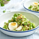 Een wit emaille bordje met blauwe rand is gevuld met de linzensalade. Het is een salade rijk aan groene groenten. Het gerecht is afgewerkt met een gekookt eitje. 