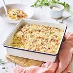 Een heerlijke gevulde ovenschotel boordevol comfortfood staat op de tafel te blinken. Onze mac and cheese met Belgische kazen zit in een witte ovenschotel met donker blauw randje, zoals bij de bomma. Er ligt een zalmroze servette langs en de een takje verse peterselie voor extra kleur in het beeld. 