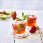 Twee roodgekleurde mojito's op de tafel, afgewerkt met verse munt en nog een aardbei. Alleen al kijken is een feestje, tijd om die cocktail te benuttigen. Het glad kreeg zelfs een suikerrandje. 