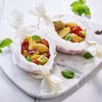 Op tafel staat een marmere serveerplank met hierop twee papillots met aardappel en kleurrijke groenten.