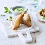 Klaargemaaakte samosa met lamsvlees liggen gepresenteerd op een marmer plankje. Ze worden opgediend met een frisgroene dip van munt en erwtjes.