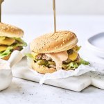 Twee heerlijke burgers liggen klaar op een marmere snijplank. Het vlees is verdeeld in twee dunne porties met de saus en gesmolten kaas er bovenop. De burgers worden recht gehouden door middel van een prikker.