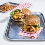 Twee hamburgers liggen op een inoxe plateau. De ene burger moet zijn hoedje nog krijgen.