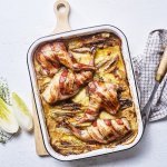 Op een grote houten snijplank staat de ovenschaal met de tartiflette en stukken konijn. Het konijn in omwikkeld met sneetjes spek, waardoor het nog iets extra heeft. Er ligt witloof langs en verse tijm.