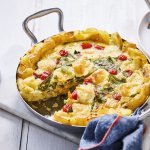 Op tafel staat een lage kookpan met hierin de klaargemaakte aardappeltortilla. Hij oogt lekker kleurrijk door de rode kerstomaatjes, groene boontjes en goudgele aardappelen. Wij schepte alvast een portie uit de kookpan op een bord. 