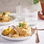 Twee borden staan klaar om van te smullen. Vol-au-vent van vis in een bladerdeegpasteitje met pommes duchesse. Er staat een glaasje water naast het bord.