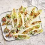 Op een rechthoekige dienschotel liggen meerdere blaadjes van witloof gevuld met een stukje sprot, ringen van sjalot en croutons. In het hoekje van de schotel liggen de roomkaasballetjes, deze balletjes zijn gerold in roze peperkorrels en verse dille waardoor ze als het ware een jasje van kruiden kregen.