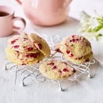 Op een kleine taartrooster liggen enkele koekjes te drogen. De koekjes hebben rode vlekjes van de framboosjes. Er staat een theepot langs met al een uitgeschonken thee in bijpassende roze tas. 