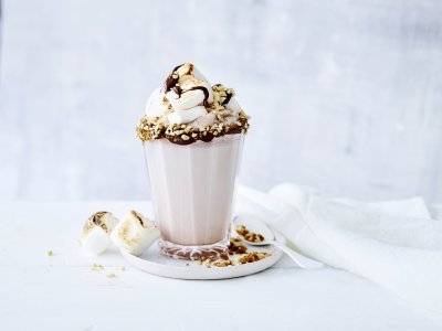 Een chocolademilkshake staat te shinen in het midden van de foto. Hij is afgewerkt met geroosterde marshmallows en vers gesmolten chocolade. Crazy shake ten top!