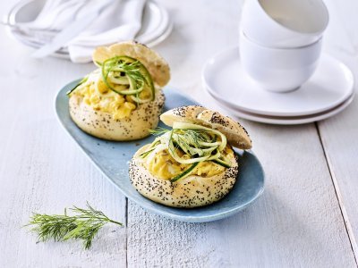 Twee pistolets liggen op een grijsblauw bordje. De pistolets zijn opengesneden en gevuld met roerei en courgetteslingers. 