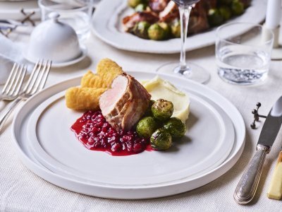 Feestelijk varkenshaasje met pastinaakcrème en geroosterde spruitjes Op een wit bord is dit feestelijk gerecht geserveerd. Eerst een schepje pastinaakcrème, met hierbij de veenbessensaus, de kroketten, spruitjes en het stukje varkensvlees. Ten aanval.