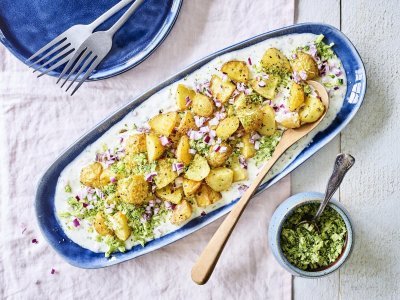 Een langwerpig blauw bord staat op tafel. Hierop is yoghurt op geschept met krokante aardappelen, stukjes rode ui en geraspte broccoli. 