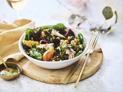 Geroosterde bietjes met een dressing van honing & mosterd Een salade van bietjes, boerenkool en spinazie afgewerkt met noten en makreel. Deze feestsalade staat op een houten plank met de dressing in een apart gouden potje.