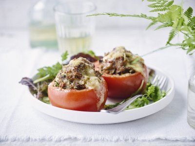 Gevulde tomaten met gehakt en gesmolten kaas op een wit bord gepresenteerd met verse sla. 