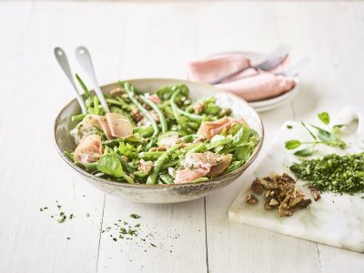 Groene salade met boontjes, paprika, erwtjes en gerookte ham Een licht groene serveerkom is gevuld met onze groene salade boordevol, jawel, groene groenten. Denk maar aan verse sla, boontjes, paprika en erwten. De salade is afgewerkt met rozige gerookte hamsneetjes en verse groene kruiden.