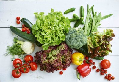 Verschillende groenten liggen op witte houten tafel die je moet eten in de zomer. Seizoensgroenten met de beste smaak en kwaliteit dus, denk maar aan sla, tomaten, venkel, paprika, komkommer, courgette en snijbonen.