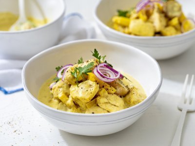 Kip curry met krieltjes Op tafel staan twee porties uitgeschept, om onmiddelijk aan te vallen met mes en vork. De curry kleurt mooi goudgeel, terwijl de rode ui voor contrast zorgt. We werken af met een takje verse peterselie voor extra kleur.