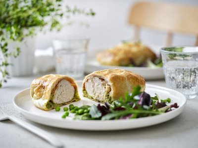 Kip wellington met gedroogde ham en erwtjespuree met munt Een mini wellington van kipfilet ligt opengesneden op een wit bord. Hierin zie je mooi een laagje erwtjespuree onder het witte vlees in het bladerdeeg pakje. Er is nog wat gemengde sla en erwtjes toegevoegd op het bord.