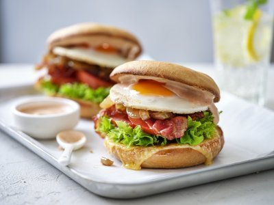 Ontbijtburger met spiegelei en spek Een burger als ontbijt, dat is er eentje met een spiegelei, spek en groentjes. Er liggen twee stuks op een schaaltje met het sausje erbij geserveerd in een potje, klaar om te proeven.