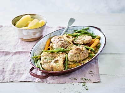 De kalfsschenkels liggen in een ovenschotel met groene boontjes en oranje wortels erbij. Dit zorgt voor een mooie variant op de klassieke ossobuco.