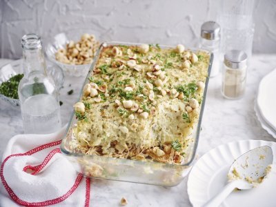 De ovenschotel met pulled chicken en knolselderpuree staat op tafel, hij is afgewerkt met hazelnoten en peterselie wat een mooie kleur geeft. Er ligt een lepel langs op een klein bordje om meteen uit te scheppen en met het hele gezin aan tafel te gaan.