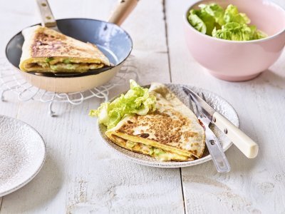 Quesadilla met een omelet en Passendale kaas Een krokante tortilla ligt in een bordje klaar om aan te vallen. Hij is gevuld met een omelet, passendale kaas, gandaham en lente-ui. De tweede quesadilla ligt nog in de pan en staat ook op de tafel.