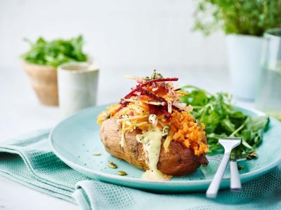 Gepofte zoete aardappel met wortelen, radijsjes, rode biet en appel Gepofte zoete aardappel met wortelen, radijsjes, rode biet en appel gepresenteerd op een blauw bord met een rucola slaatje als bijgerecht.