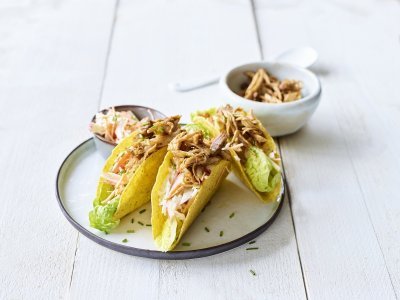 Taco met traaggegaarde varkensspiering en een koolsalade Krokante taco's liggen op een bordje, ze zijn gevuld met stukjes varkensvlees en een slaatje van kool.