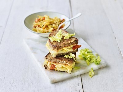 Toast met kazen van bij ons, kimchi en chilisaus Een heerlijke cheesy toast ligt op een marmere snijplank. De toast is gevuld met 2 Belgische kazen, kimchi en chilisaus.