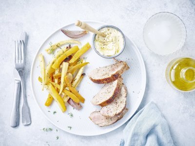 Varkenshaasje met geroosterde groenten en truffelmayonaise Groot wit bord met 4 stukjes versneden varkenshaasje, geroosterde pompoen en zoete aardappel. Er staat een klein grijs potje op het bord met truffelmayonaise is en houten lepeltje. Het bordje is afgewerkt met verse tijmblaadjes en een licht blauwe servet langsheen het bord.